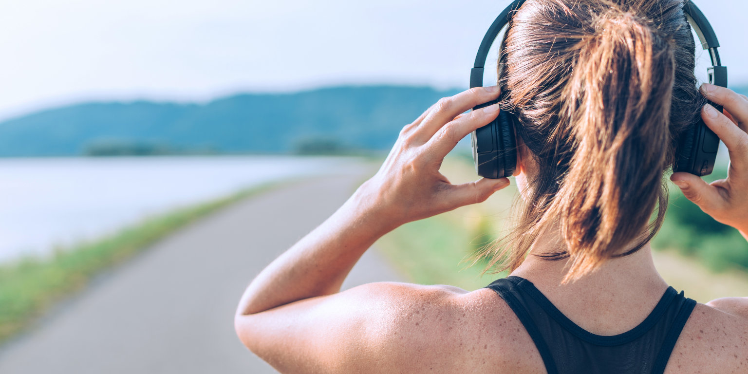 Junge Frau mit On-Ear-Kopfhörern vor Weg durch Landschaft