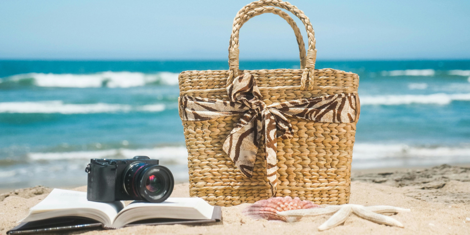 Kamera liegt auf einem Buch am Strand neben einer Tasche